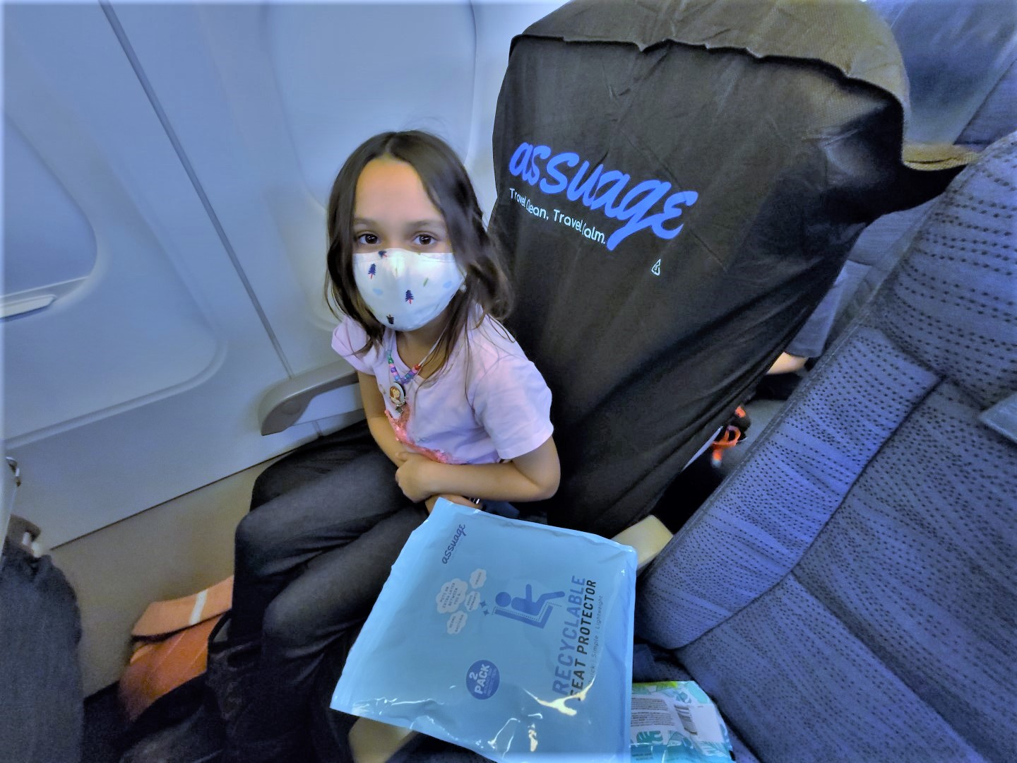 masked girl seated on assuage seat protector on flight