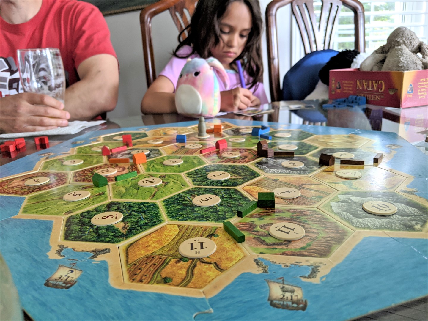 Child and stuffy in front of family board game Catan