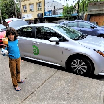 boy holding drink in front of Communauto car sharing in Toronto Beaches