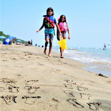 two kids walking along beach with footprints behind them