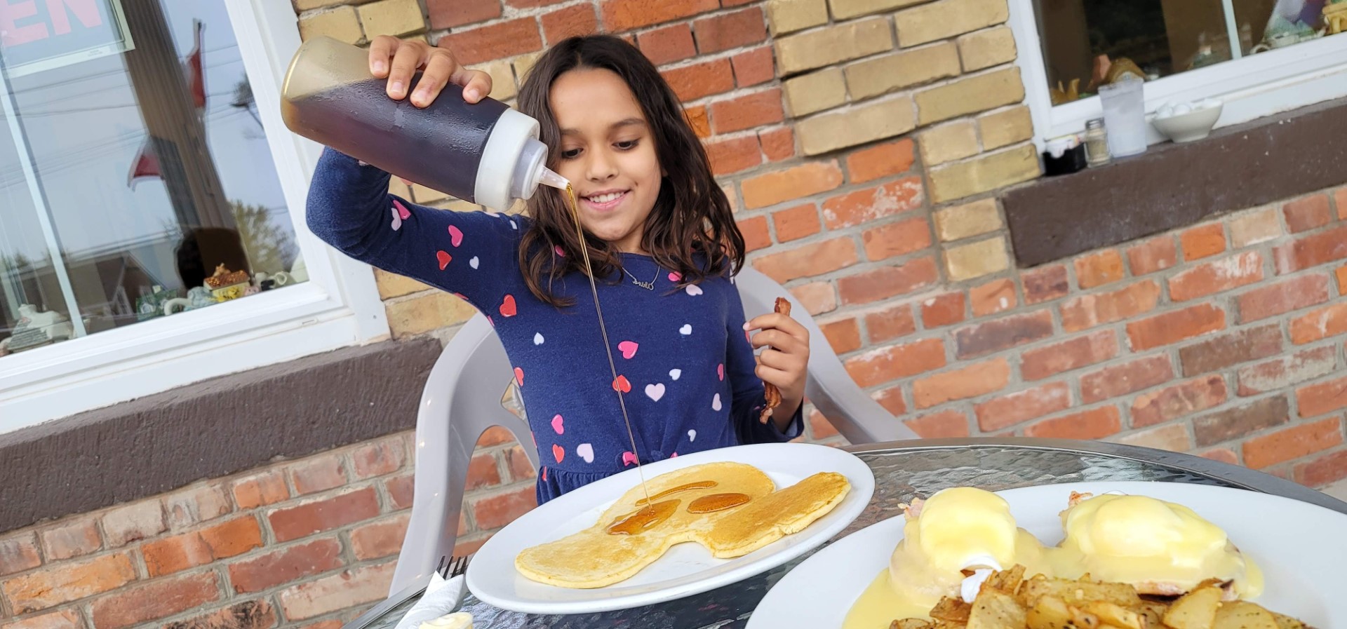 girl pouring maple syrup on mickey mouse pancakes