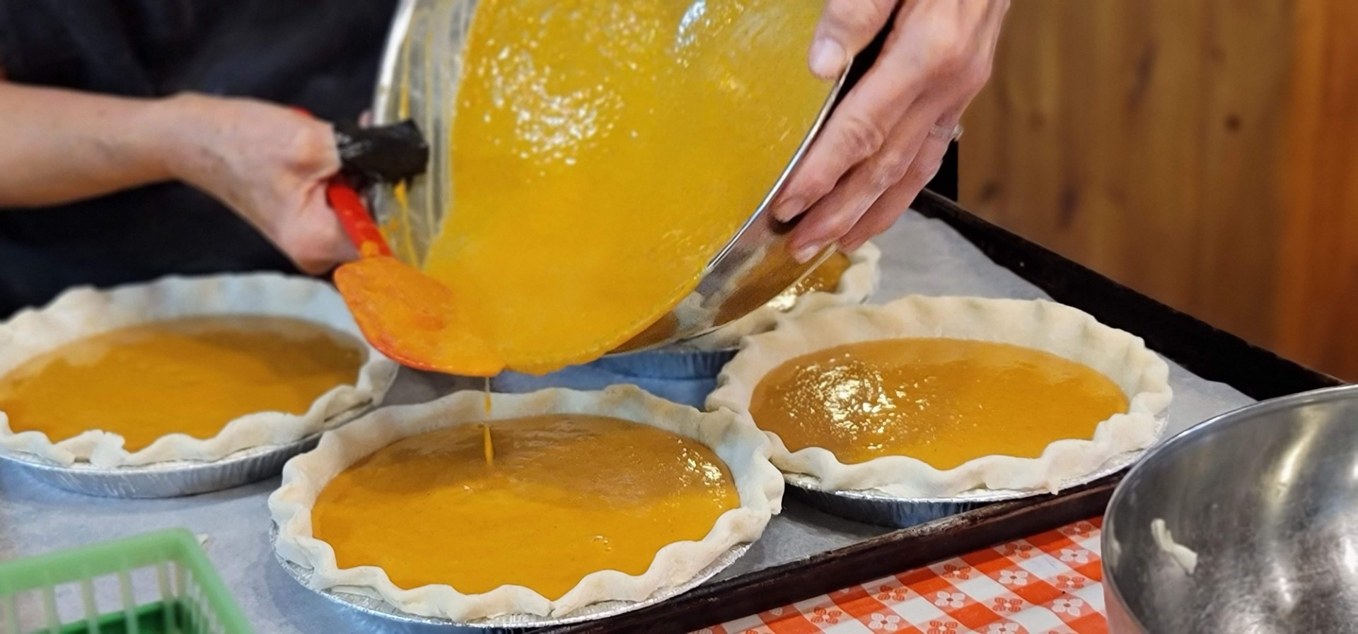 hands holding bowl pouring pumpkin into pie shell
