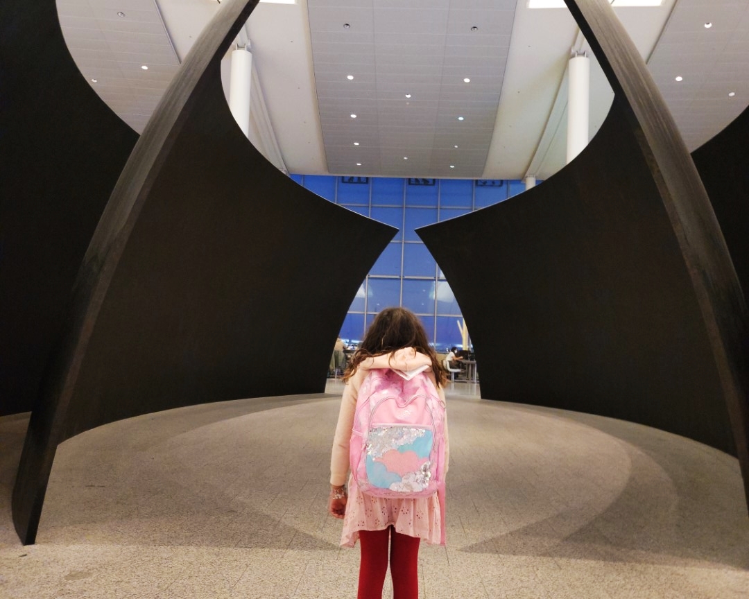 Child with pink backpack staring out at Pearson Airport