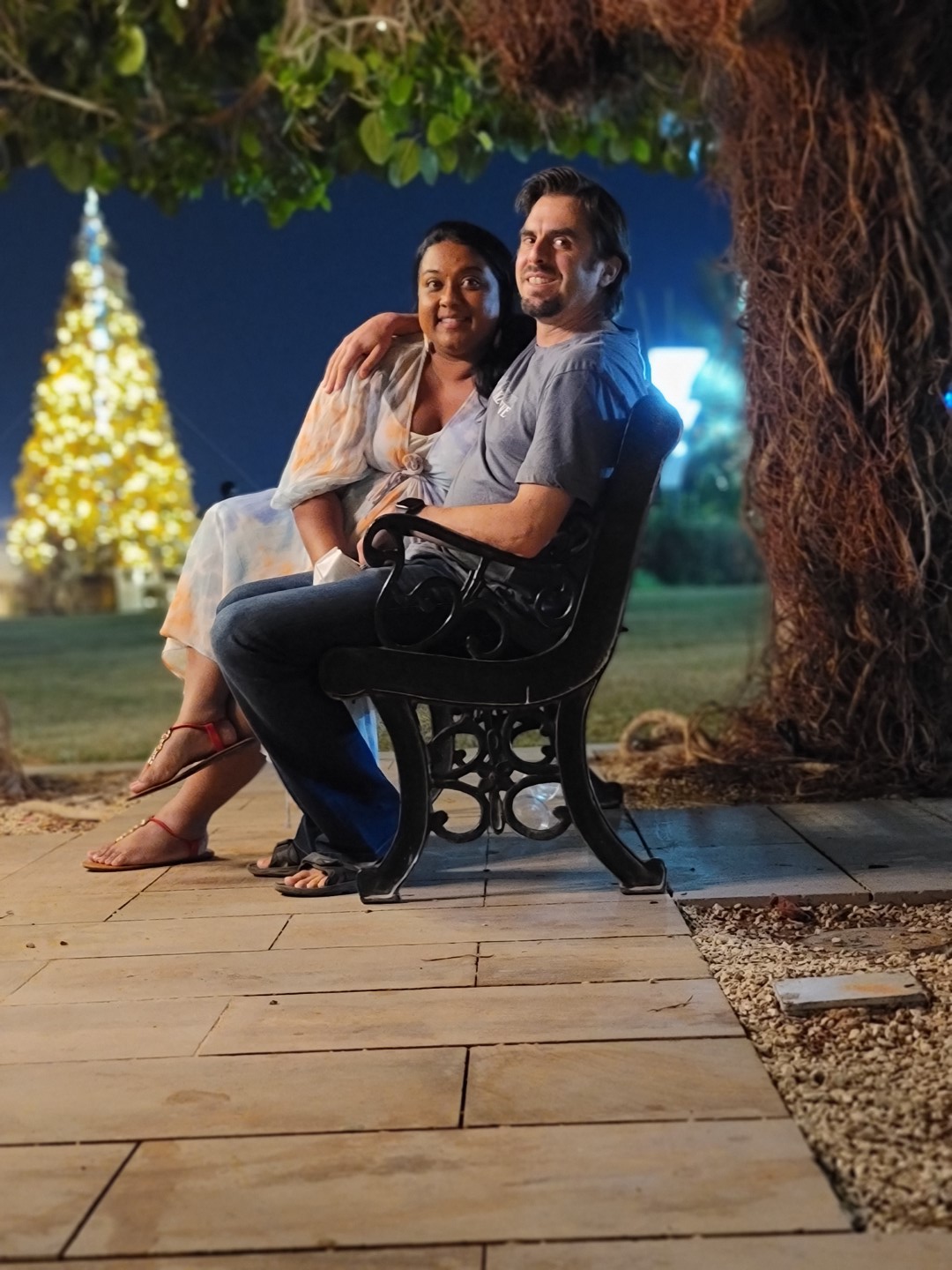 mixed couple sitting under a tree with a christmas tree