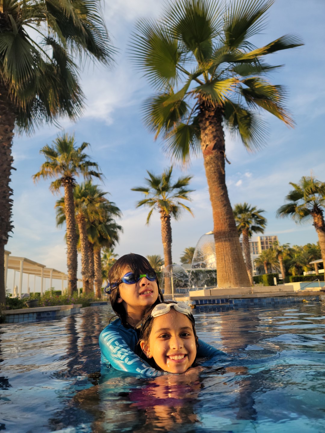 two kids in pool with blue skies and date palms
