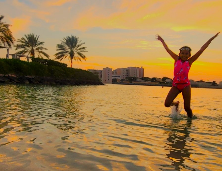 child in pink swimsuit jumping in water during sunset