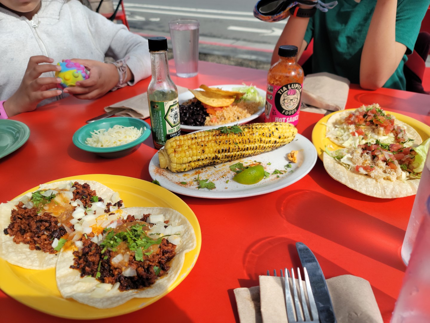 Mexican food on plates on top of red table cloth with hot sauce bottles nearby
