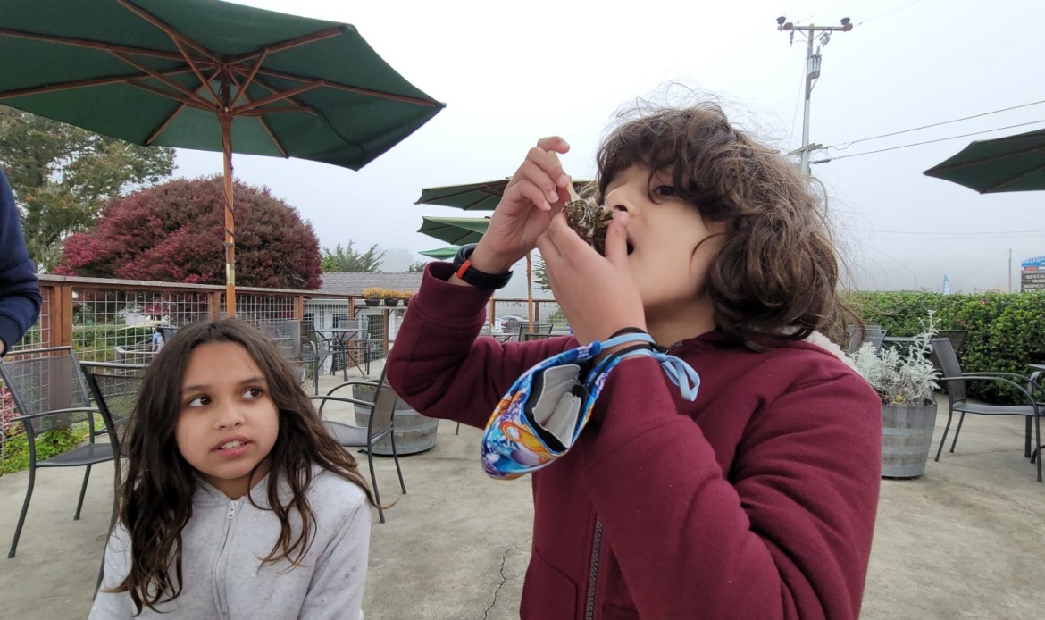 kid eating an oyster with mask in hand at Bodega Bay