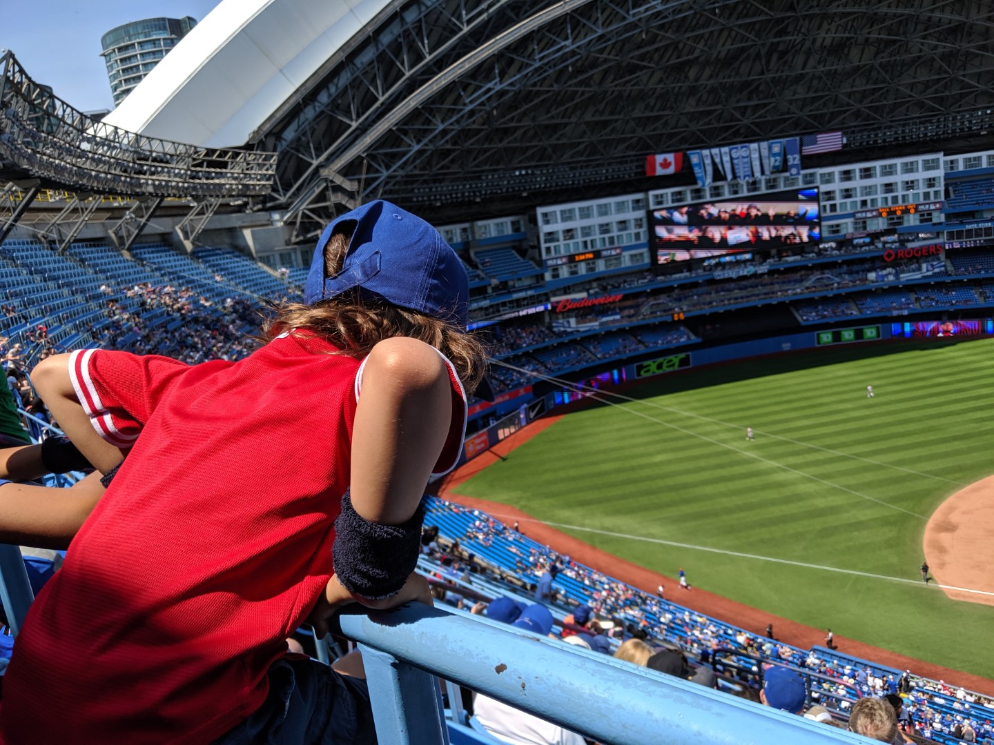 kid in red shirt and blue hat leaning over at Blue Jays game in Toronto