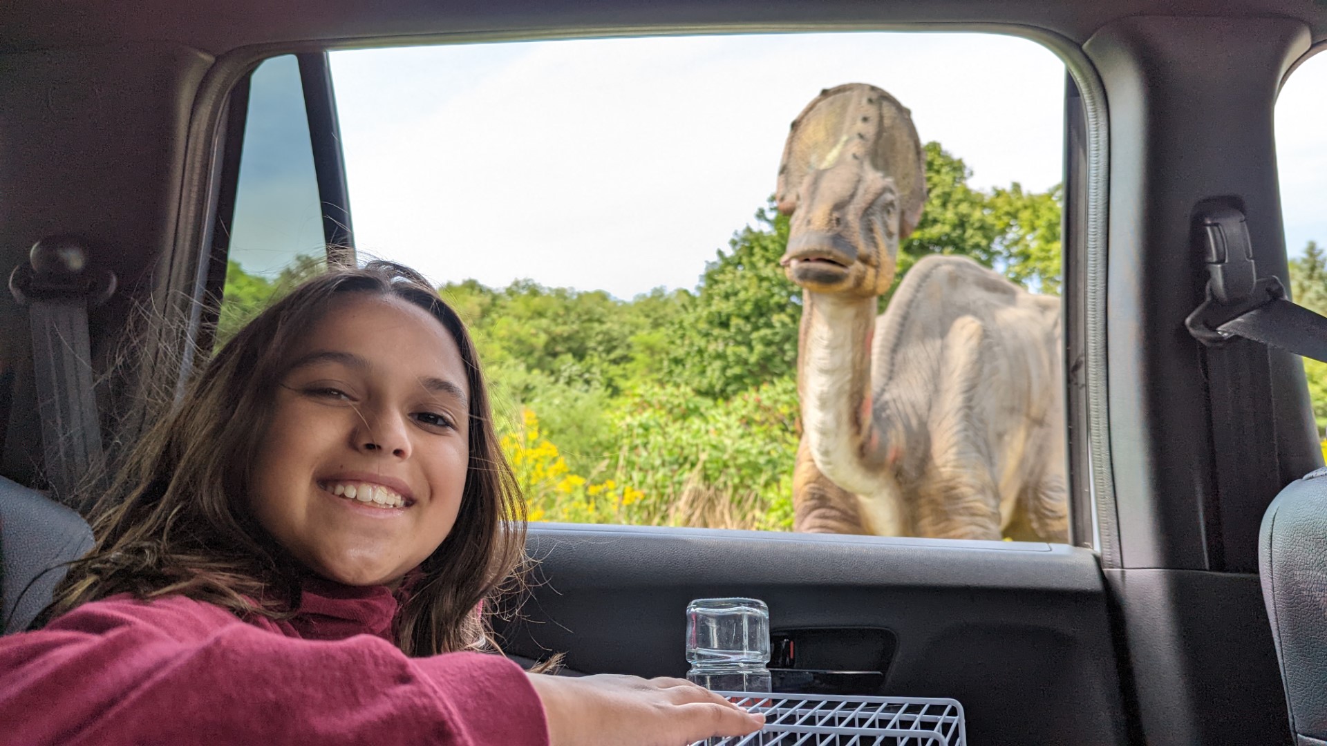 girl in car with dinosaur looking in