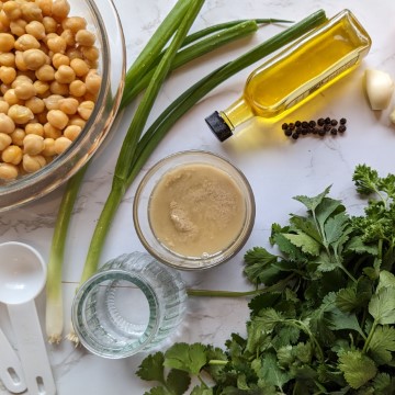 chickpeas , tahina, greens and oil on white table
